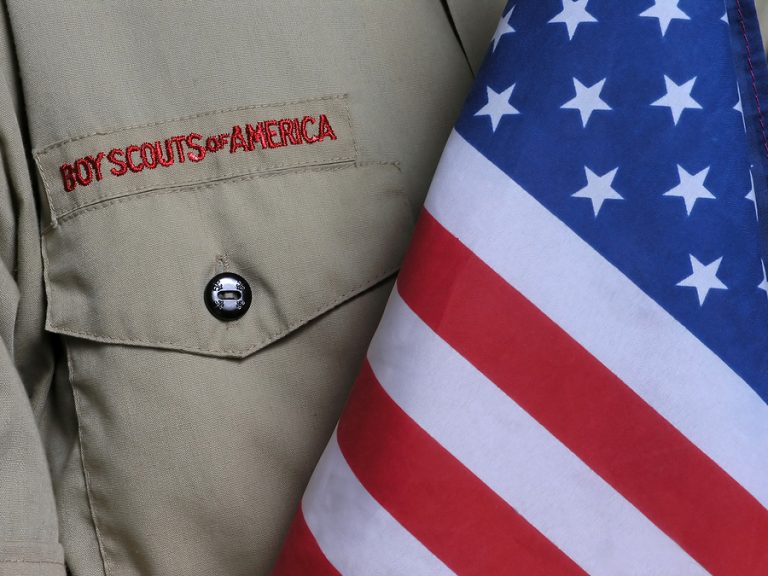 Image of a Scout shirt draped next to part of the stars and stripes flag of the USA
